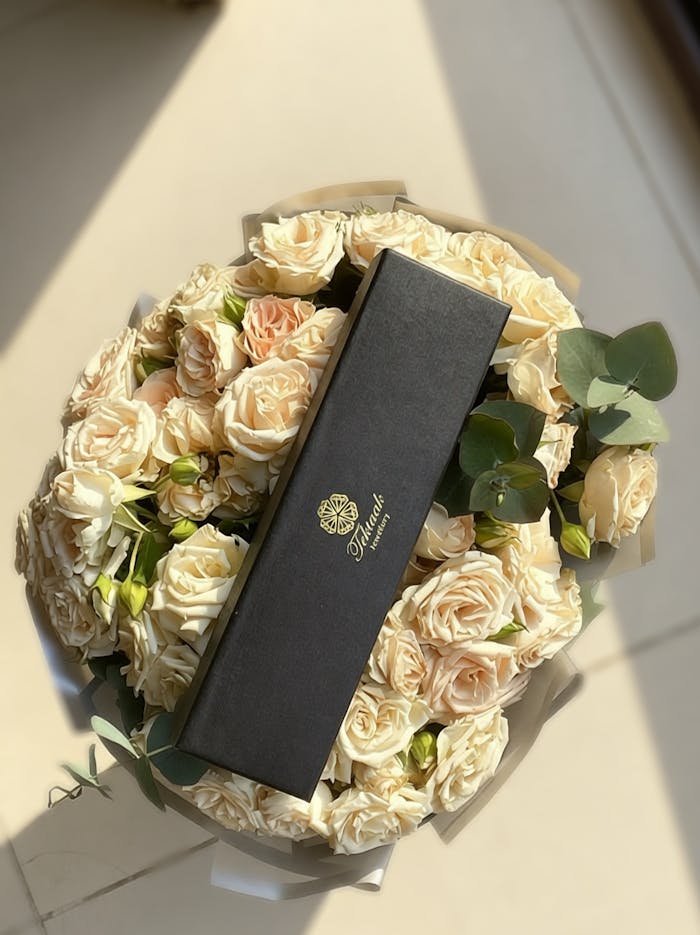 Top view of a bouquet filled with beige roses and a stylish black gift box, perfect for special occasions.